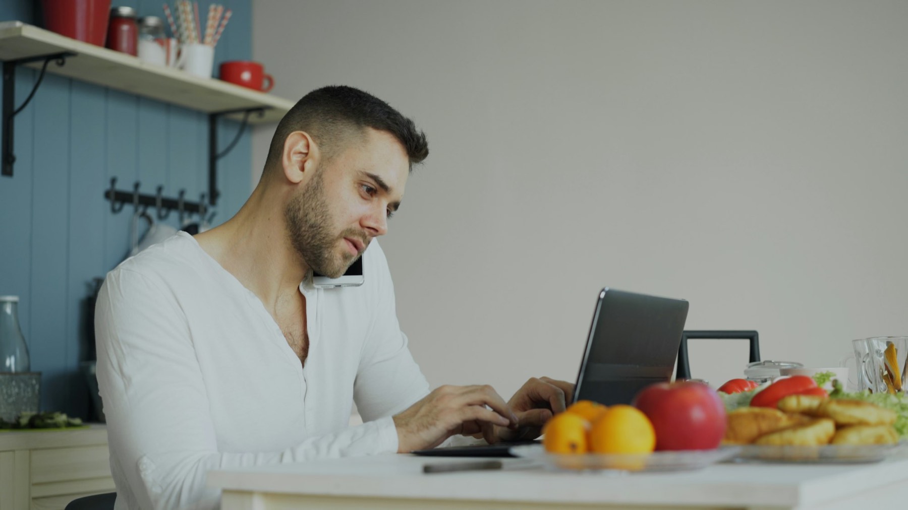 A man at a kitchen table with a laptop and a phone