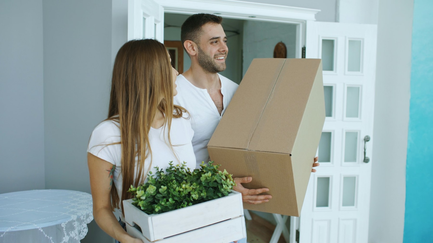 A couple carrying boxes and a plant into a new home
